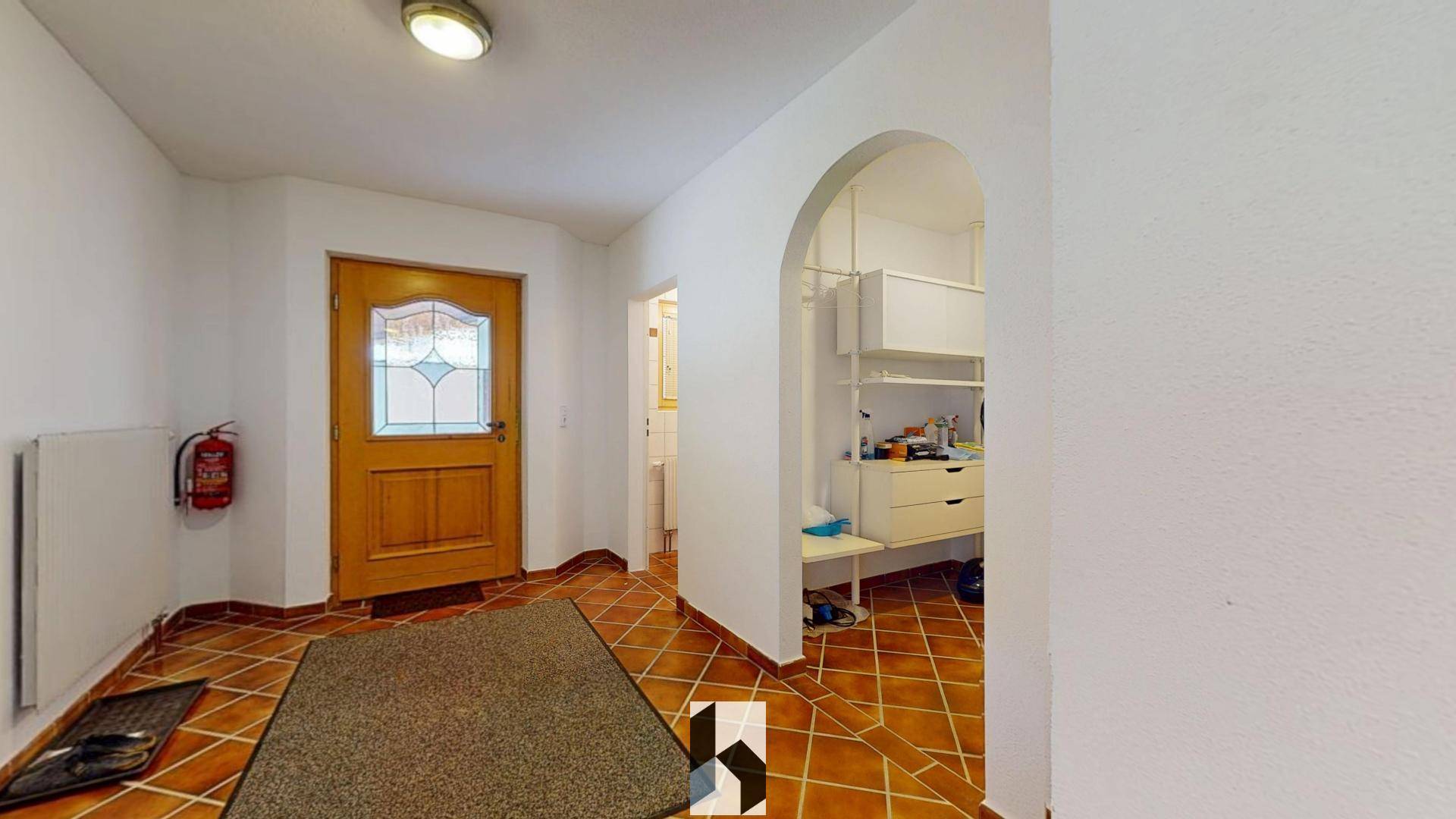 Eingangsbereich mit Terrakottafliesen, Holztür und einem praktischen Einbauschrank.