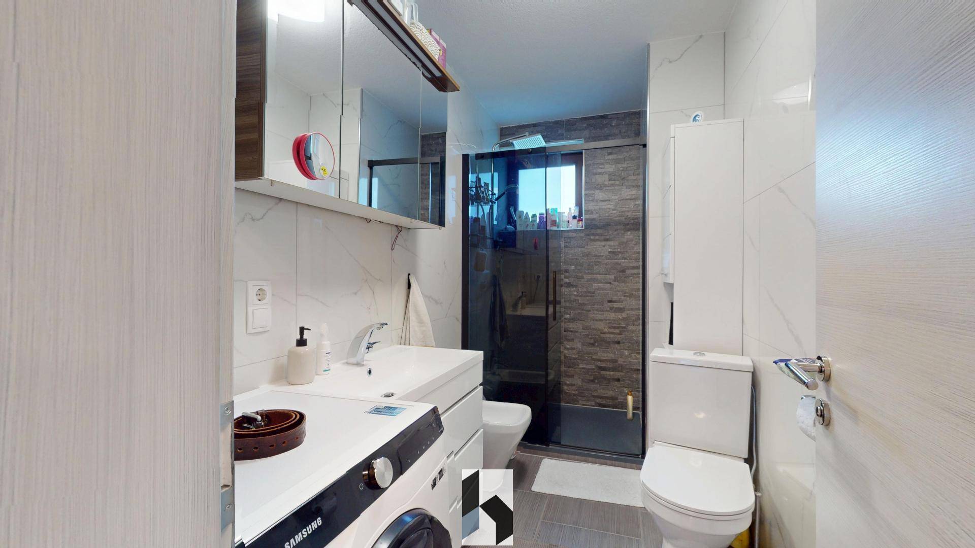 Modernes Badezimmer mit Dusche, Waschbecken, WC und integrierter Waschmaschine.