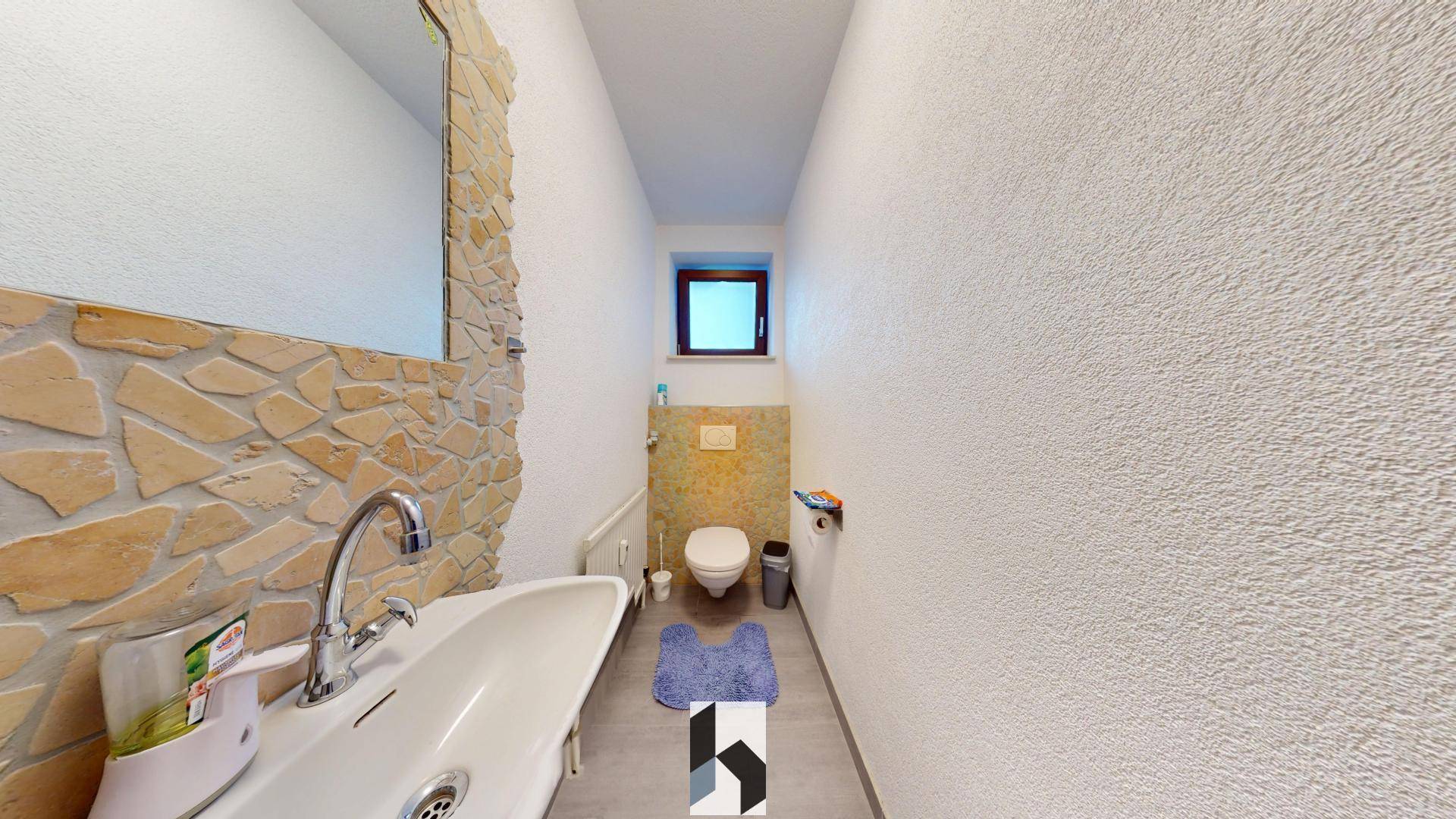Kleines Gäste-WC mit Waschbecken, Toilette und dekorativer Steinwand hinter dem Spiegel.