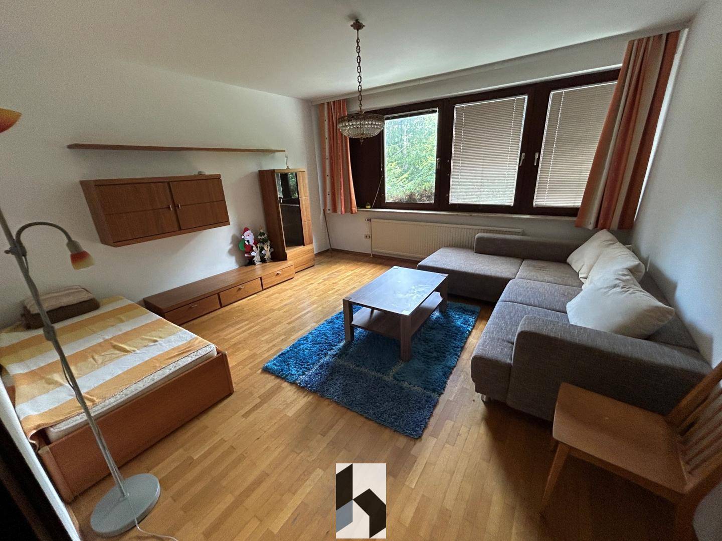 Wohnzimmer mit Parkettboden, Sofa, Bett und Holzmöbeln, bietet eine wohnliche Atmosphäre.