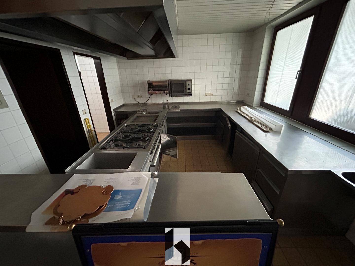 Professionelle Industrieküche mit Edelstahlflächen, Gaskochfeld und großer Dunstabzugshaube.