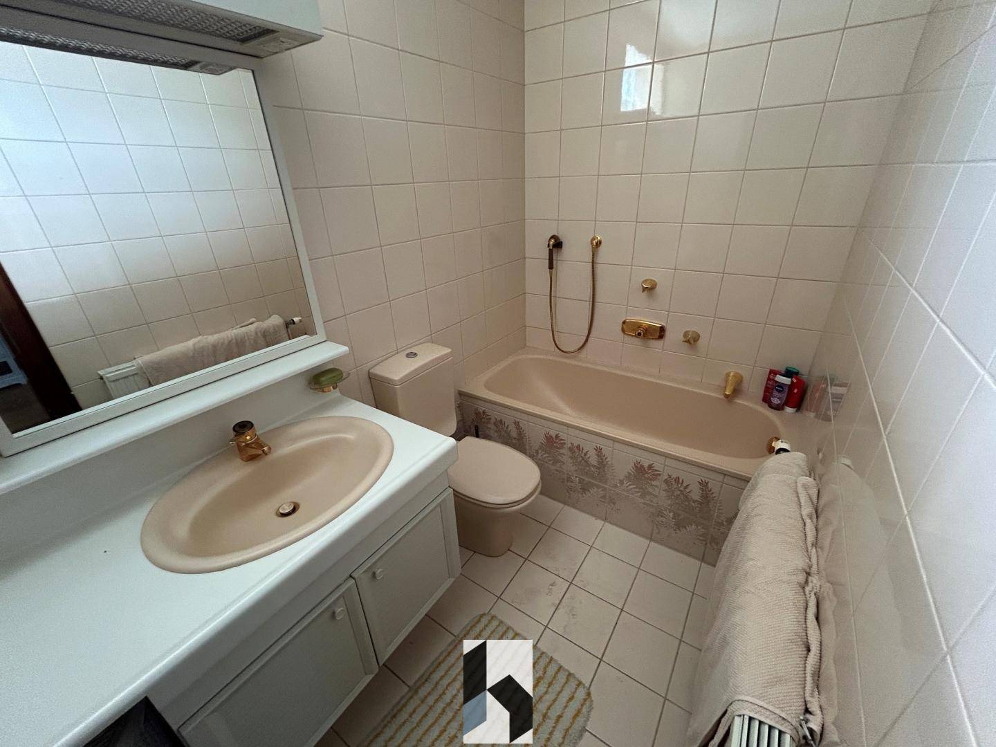 Badezimmer mit beigefarbenen Fliesen, Badewanne, Toilette und Waschbecken im älteren Stil.