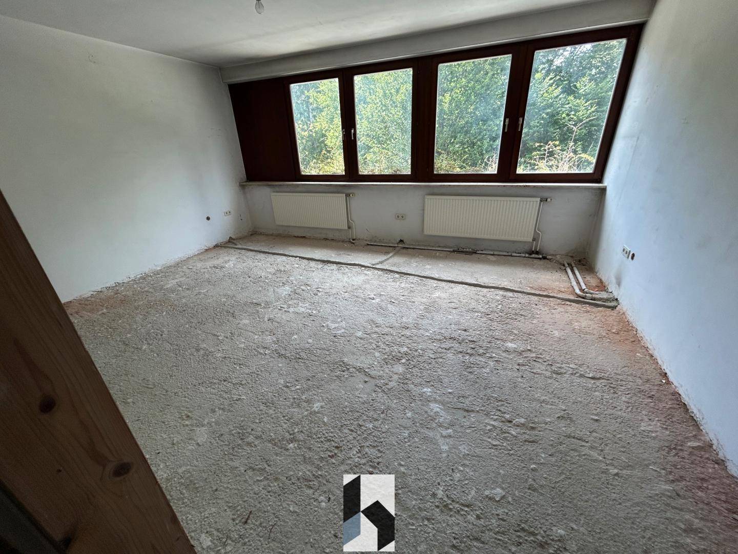 Weiterer Raum im Rohzustand mit Betonboden und Fenstern, bietet viel Gestaltungspotenzial.