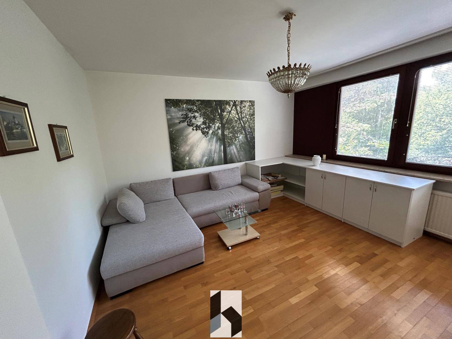 Gemütliches Wohnzimmer mit Parkettboden, Ecksofa, Couchtisch und einem eleganten Kronleuchter.