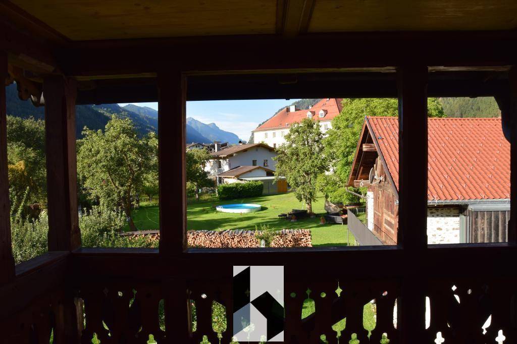 Balkon mit traditionellem Holzgeländer und weitem Blick auf die Berge und umliegende Häuser.