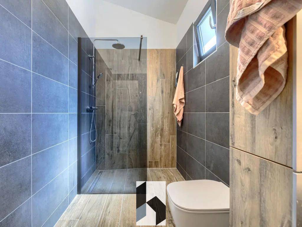 Geräumiges Badezimmer mit großer begehbarer Dusche, Wand-WC und Fenster für Tageslicht.