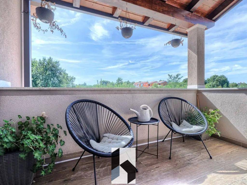 Überdachter Balkon mit bequemen Sitzgelegenheiten und Blick ins Grüne.