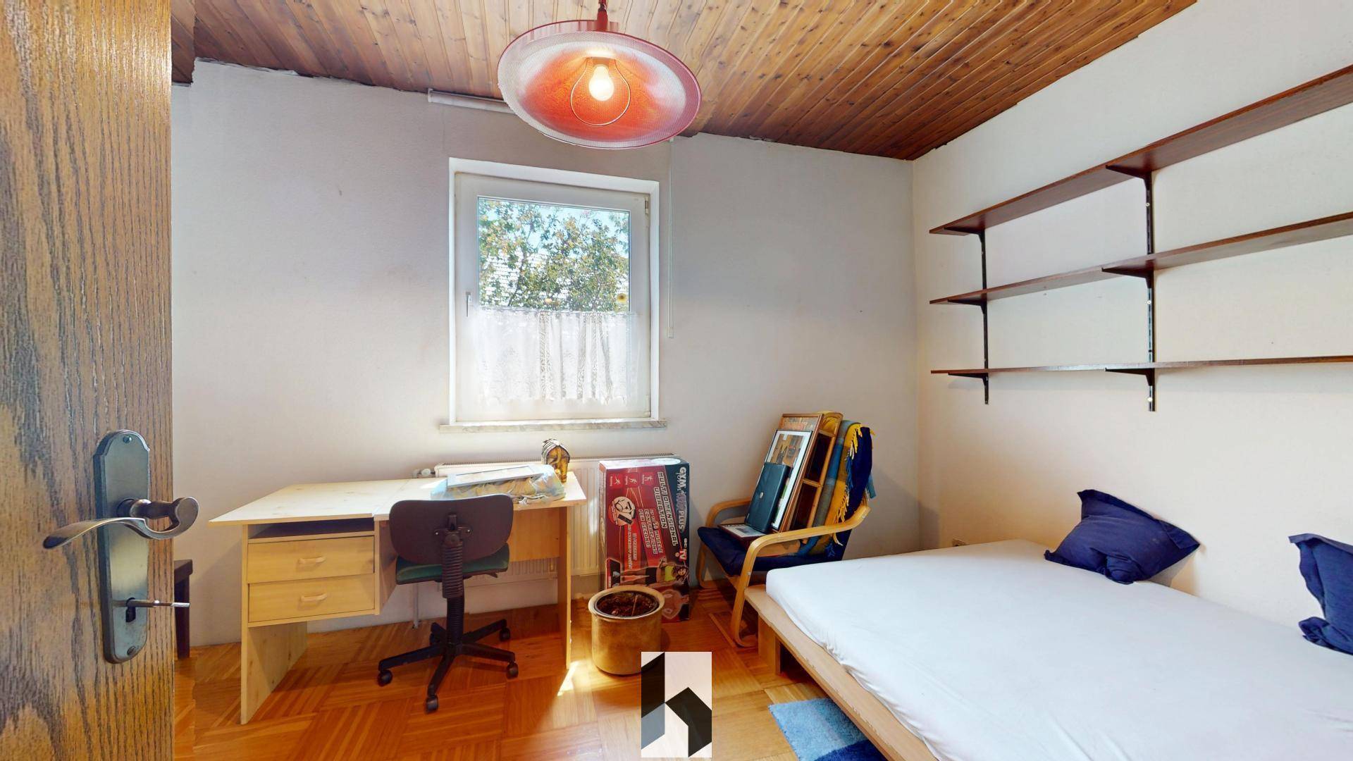 Gemütliches Schlafzimmer mit Bett, Schreibtisch, Wandregalen und einem Fenster für Tageslicht.