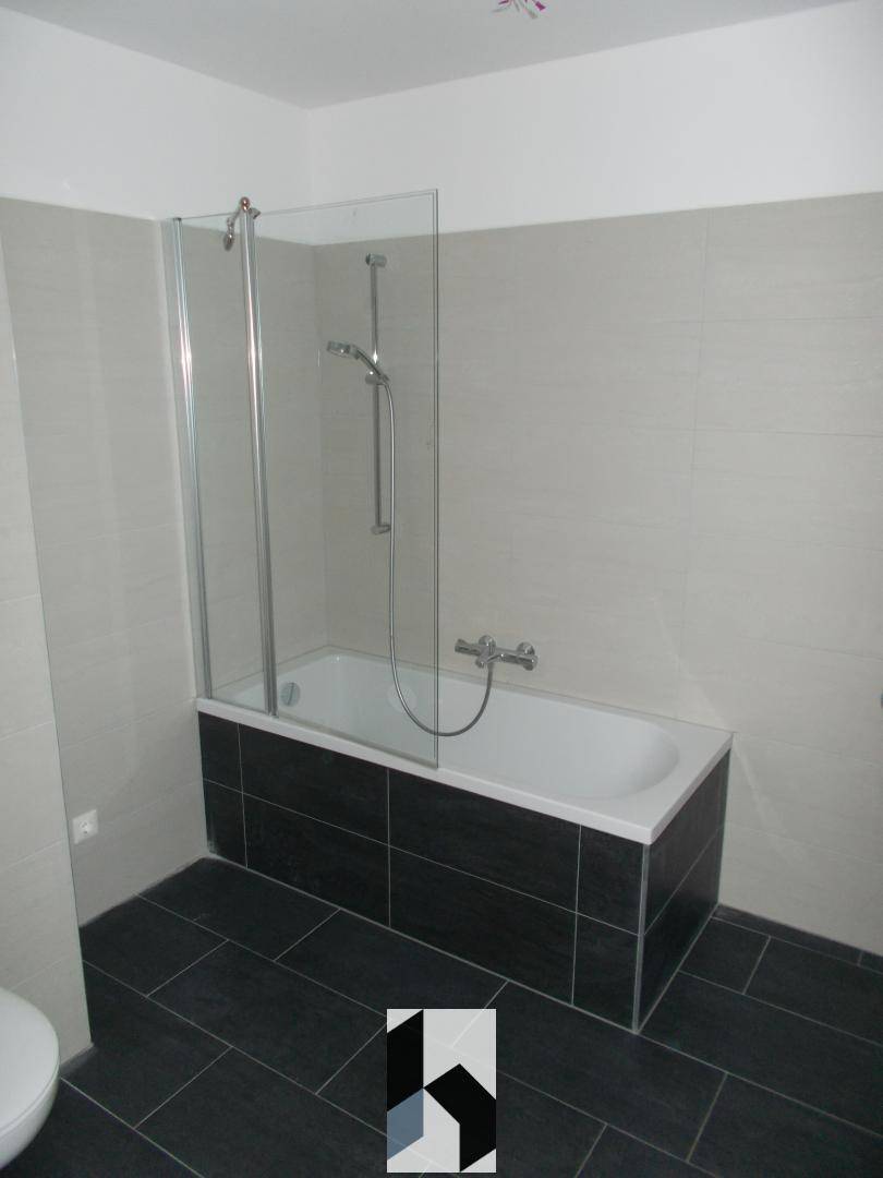 Modernes Badezimmer mit Badewanne, Duschwand und dunklen Bodenfliesen.