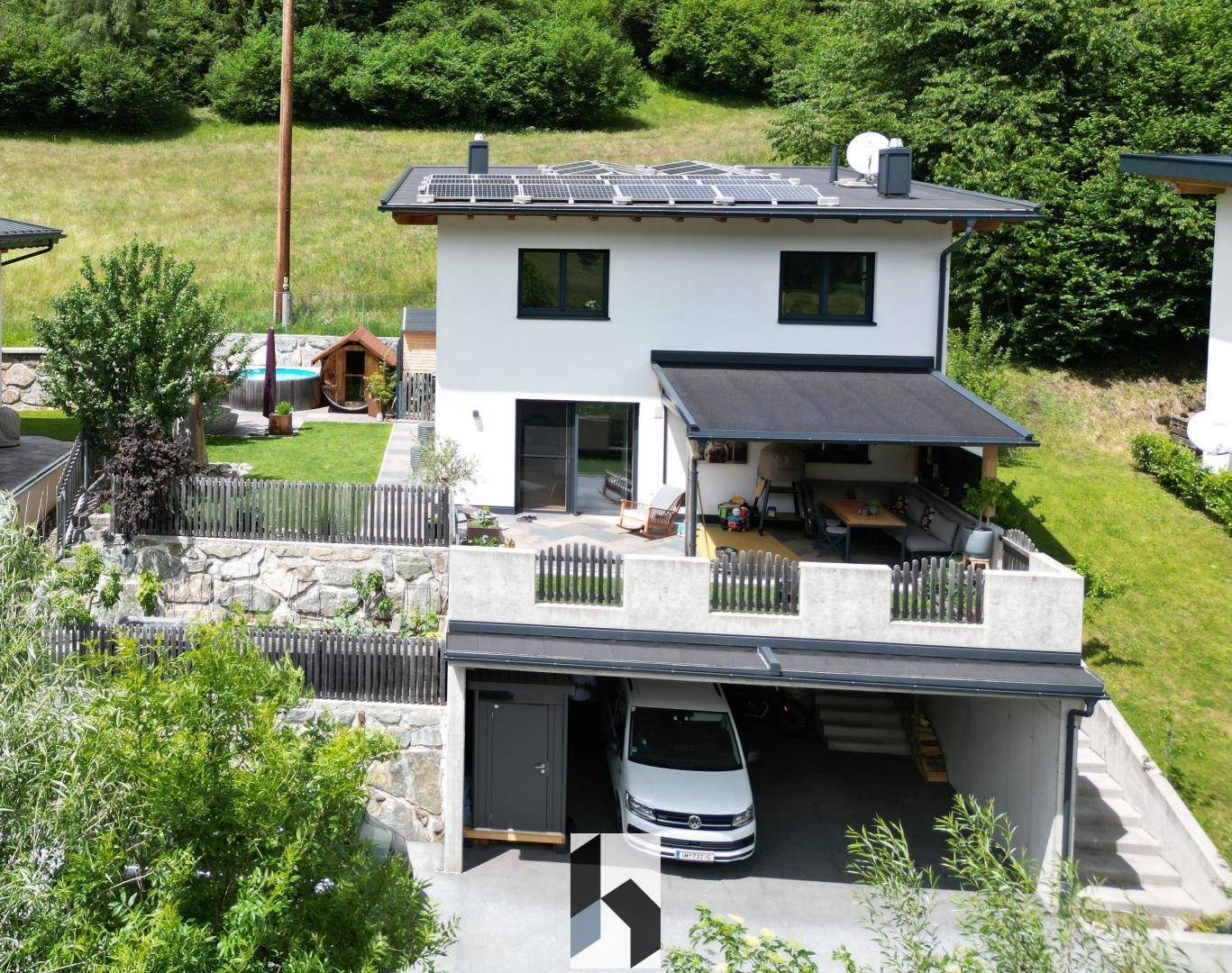 Modernes Einfamilienhaus mit Photovoltaikanlage, Garten und überdachtem Carport in alpiner Umgebung.