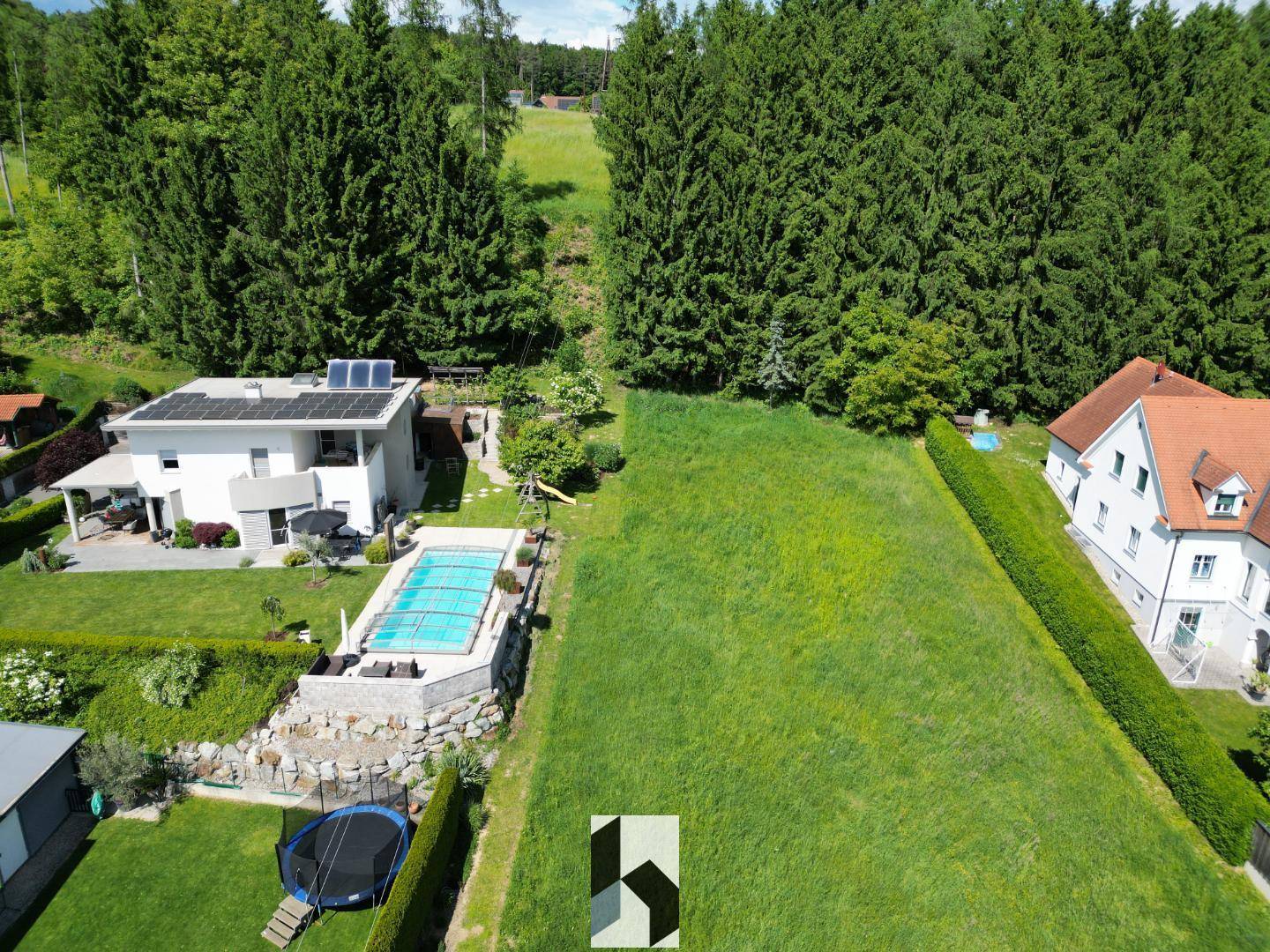Luftaufnahme eines grünen Grundstücks neben einem Haus mit Pool, Solaranlage und Trampolin.