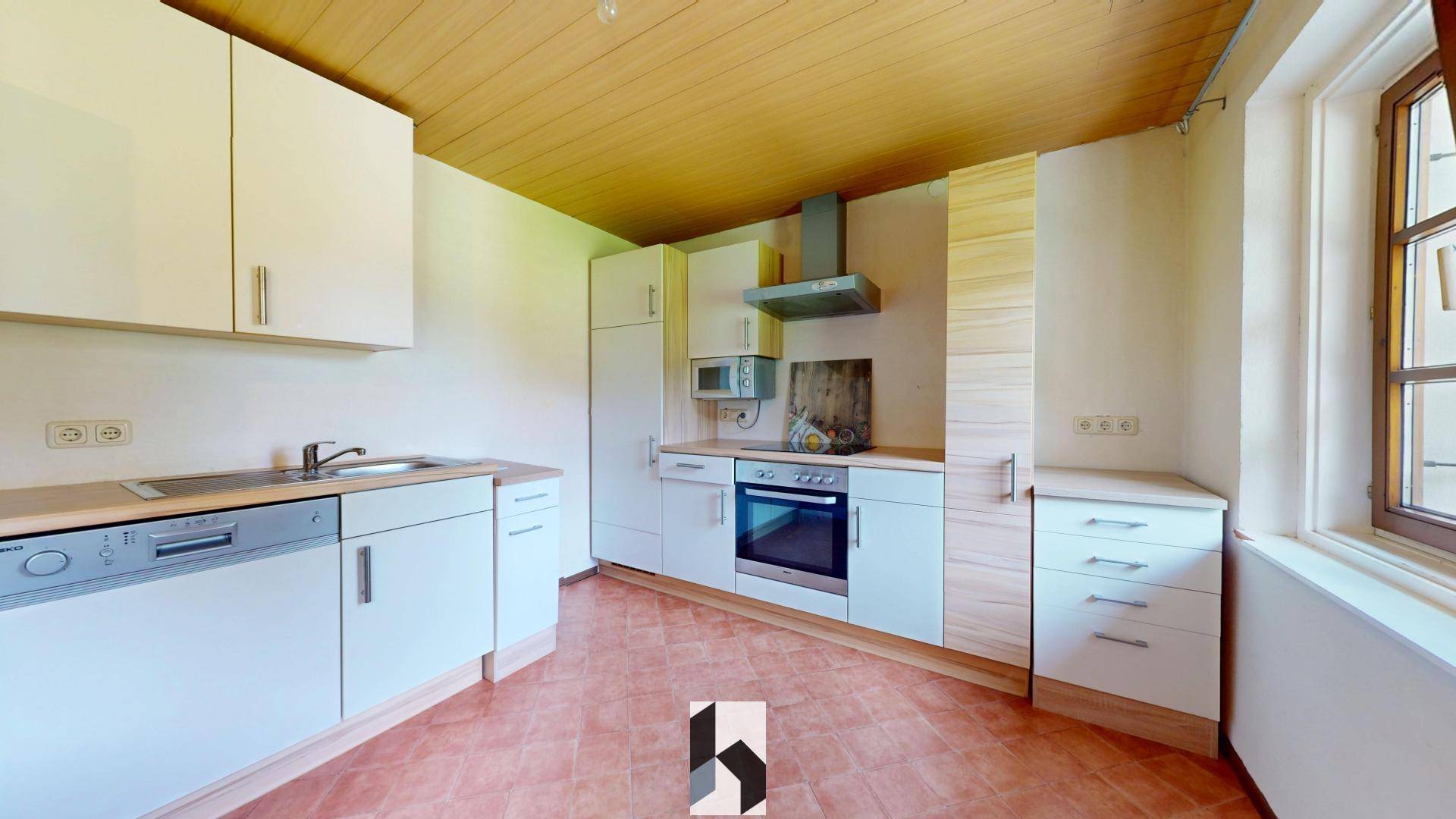 Helle Küche mit weißen Schränken, Holzdecke und Terrakotta-Fliesenboden, ausgestattet mit grundlegenden Geräten.