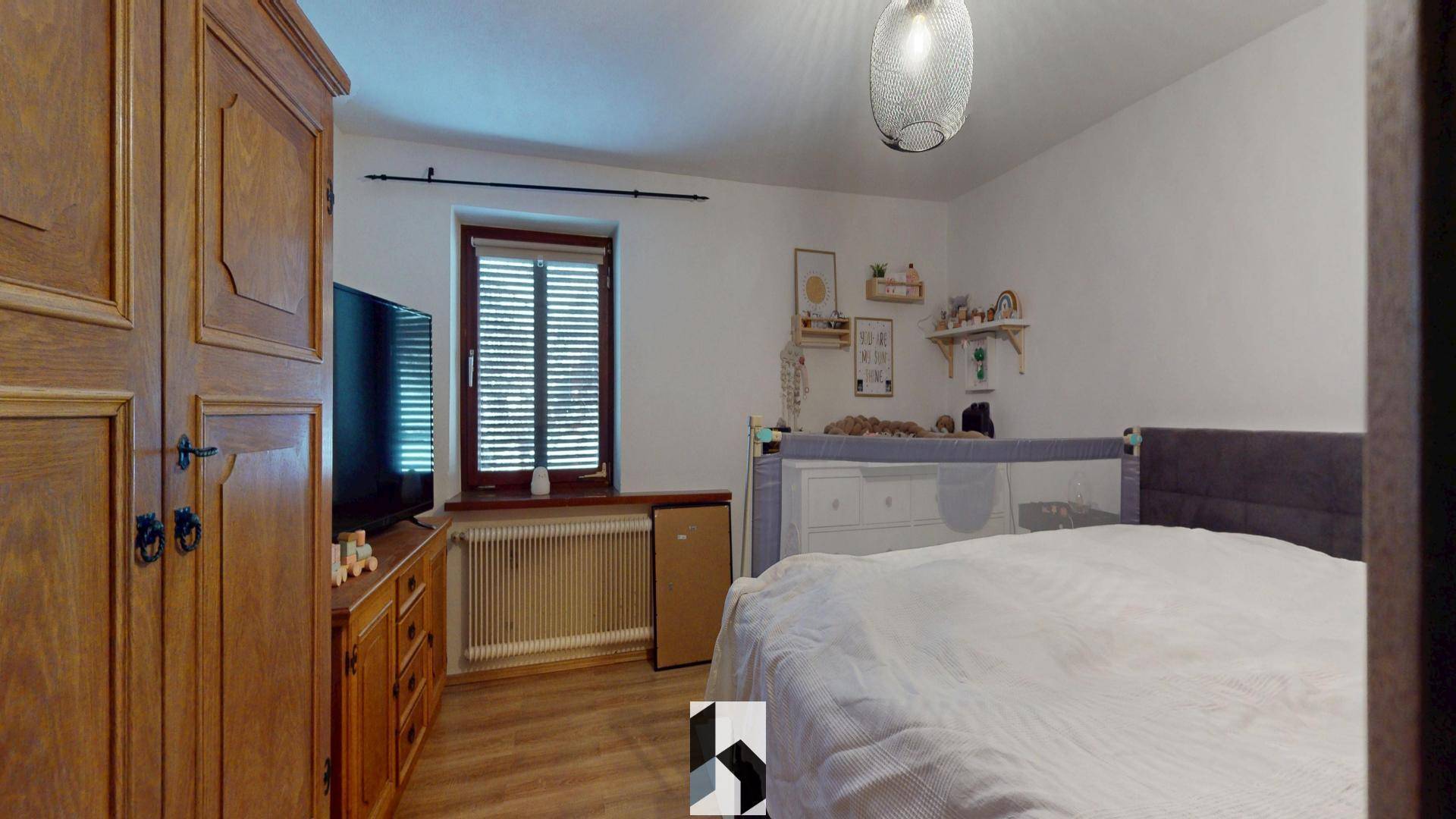 Gemütliches Schlafzimmer mit Holzkleiderschrank, Doppelbett und Fenster mit Jalousien.