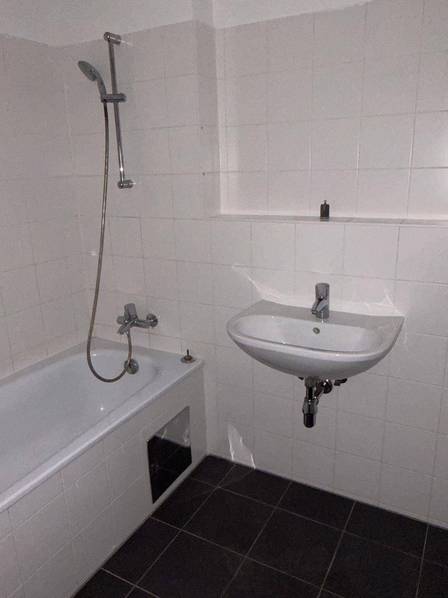 Funktionales Badezimmer mit Badewanne, Duschvorrichtung und einem einzelnen Waschbecken.