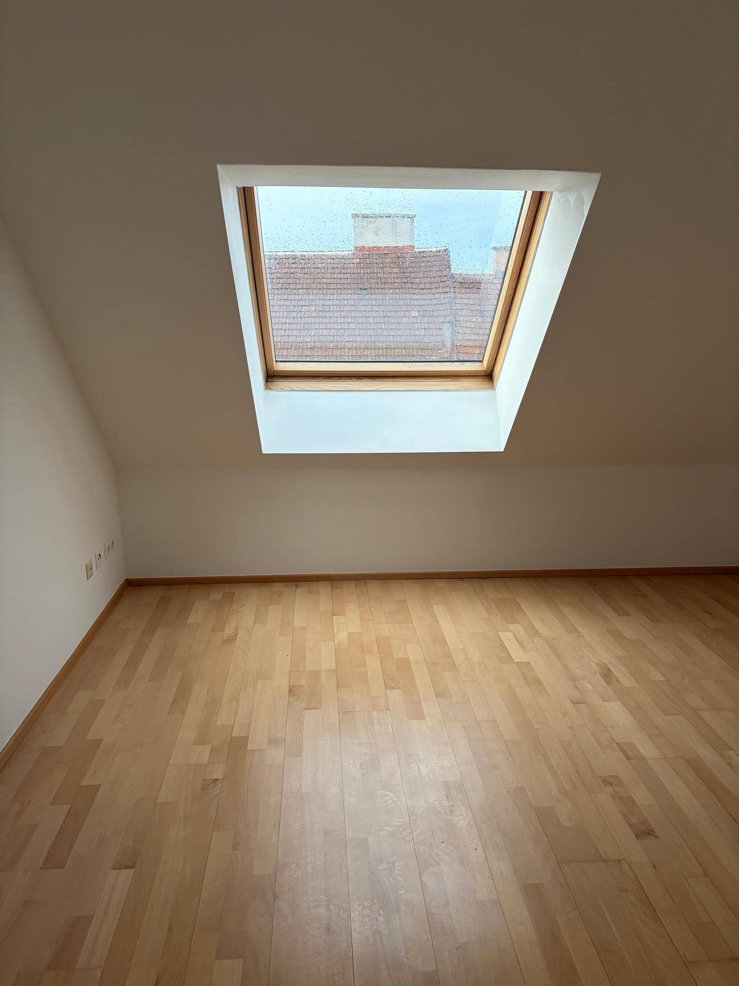 Lichtdurchfluteter Raum im Dachgeschoss mit Holzboden und einem großen Dachfenster für optimale Belichtung.