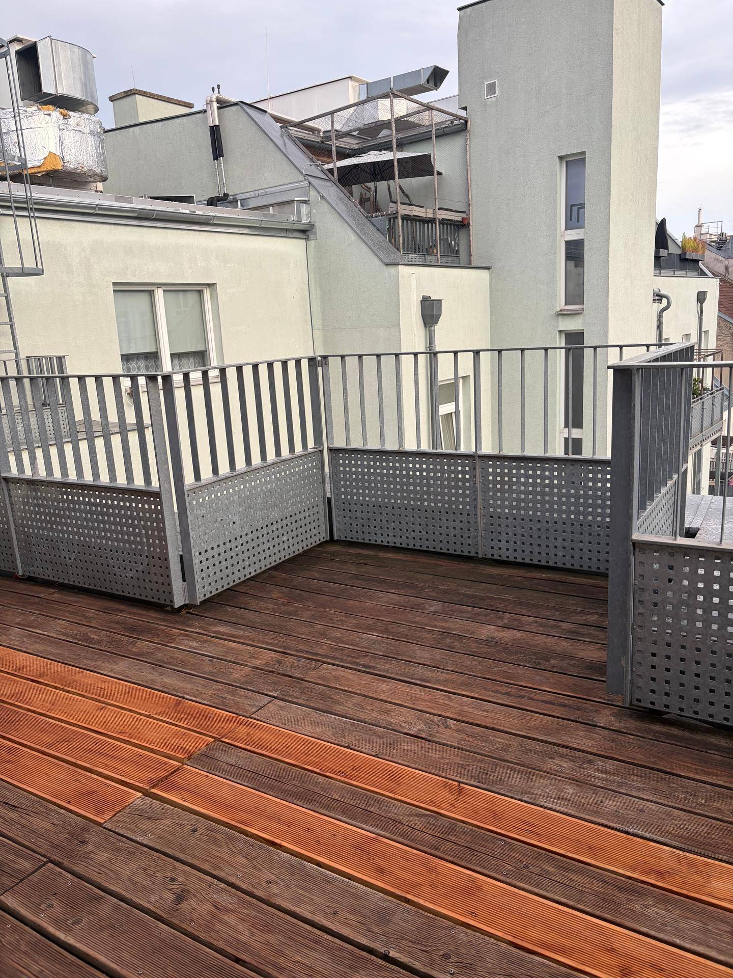 Geräumige Dachterrasse mit Holzdielen und Metallgeländer, umgeben von städtischer Architektur.