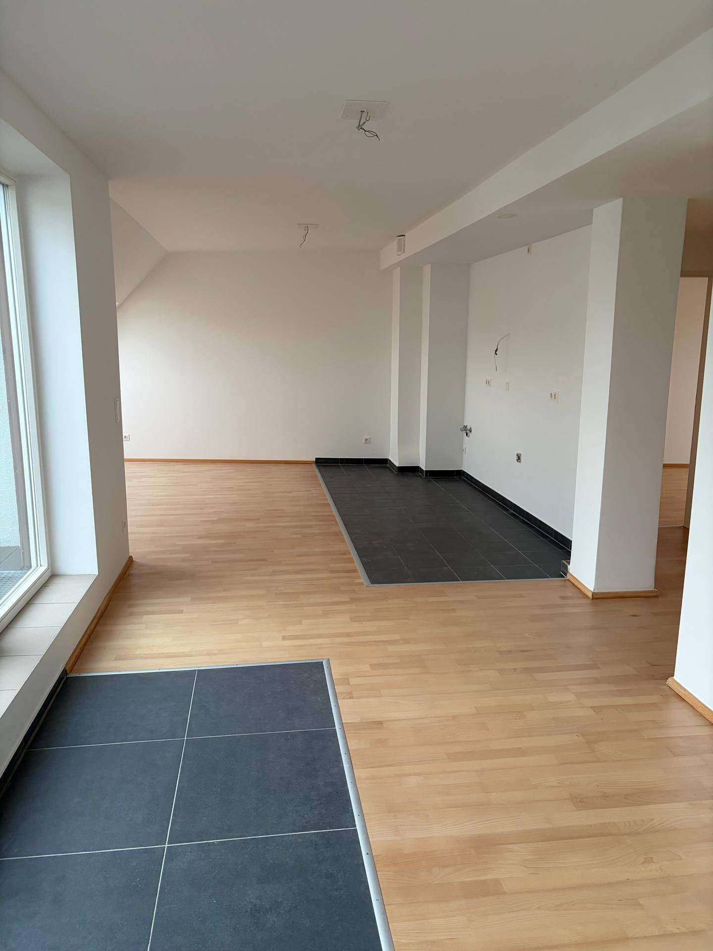 Geräumiger, heller Wohnbereich mit Holzboden und einem gefliesten Bereich, ideal für eine offene Küche.