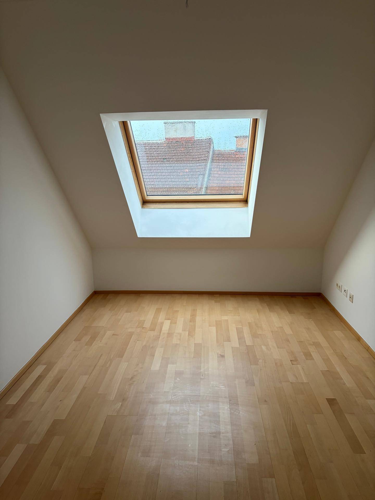 Helles Dachzimmer mit Holzboden und einem großen Dachfenster, das viel Tageslicht hereinlässt.