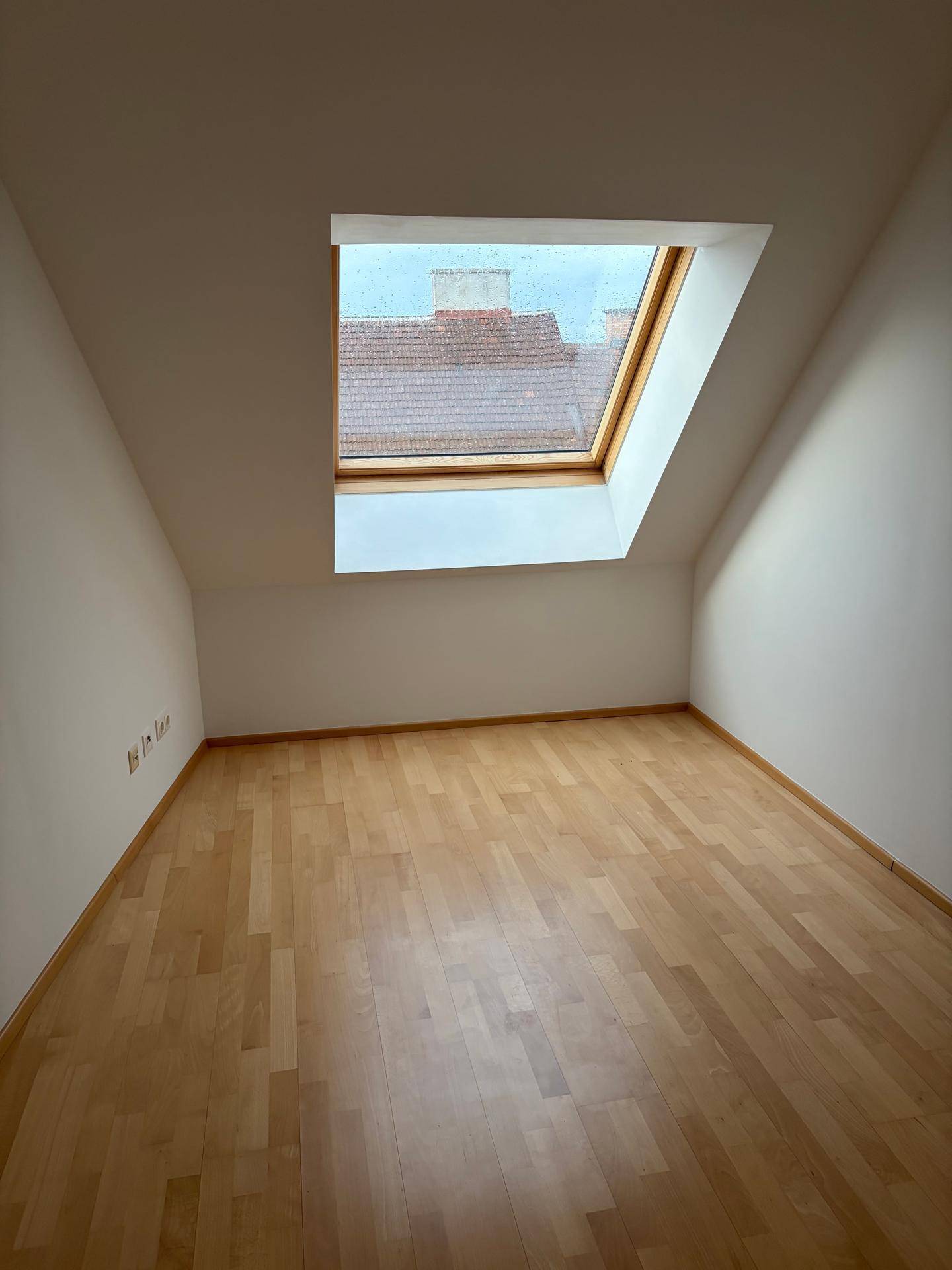 Gemütliches Zimmer im Dachgeschoss mit schrägen Wänden, Holzboden und einem großen Dachfenster.