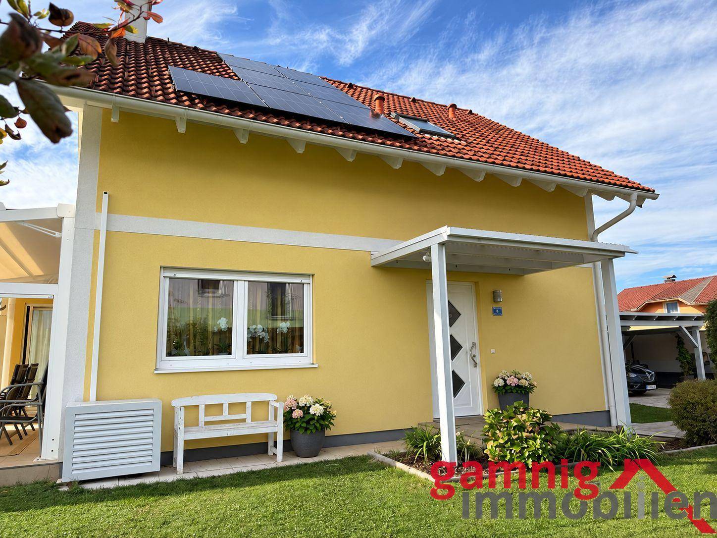 Eingangsbereich des gelben Einfamilienhauses mit Vordach und Solaranlage auf dem Dach.
