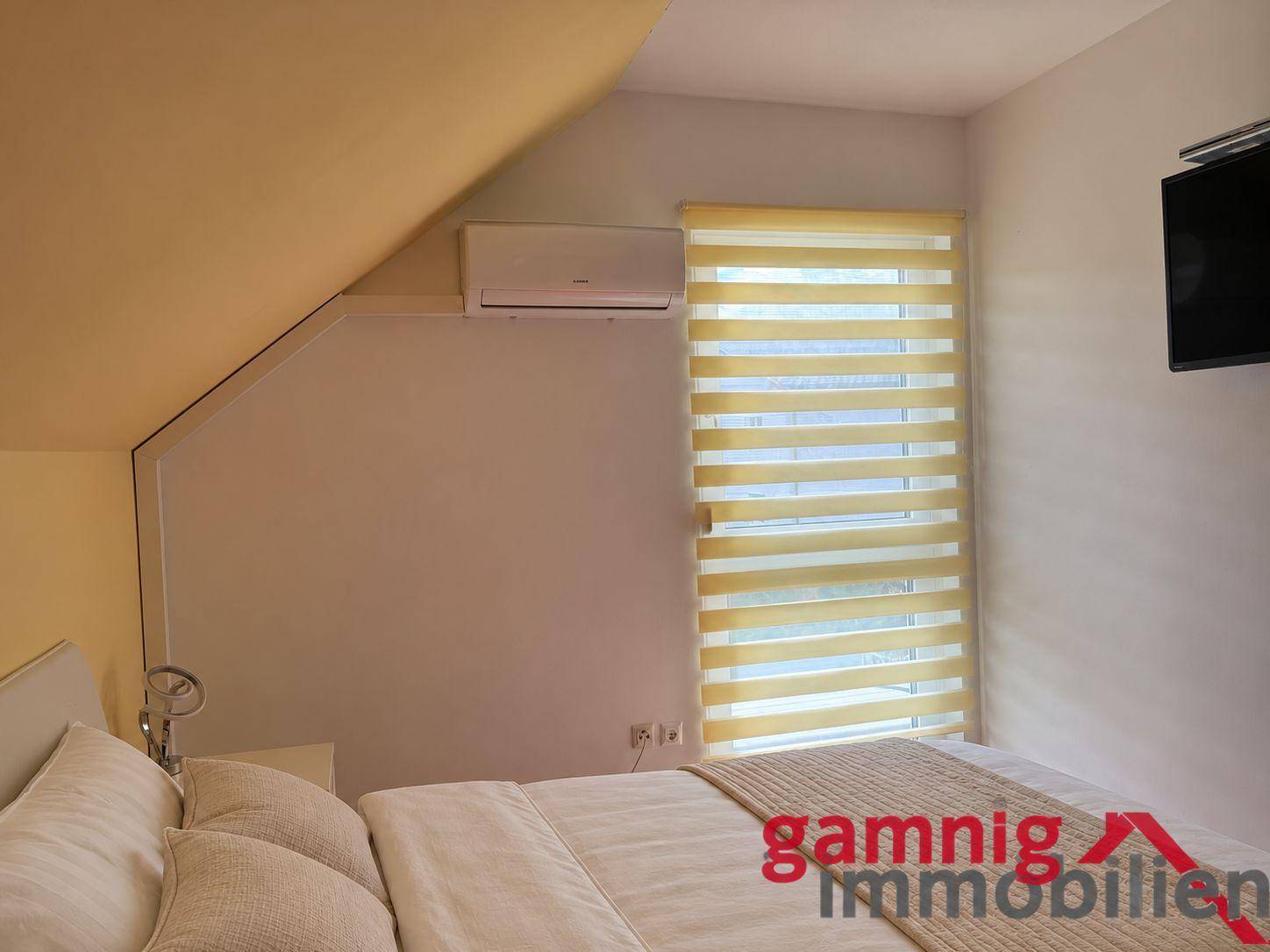 Gemütliches Schlafzimmer im Dachgeschoss mit Schräge, Klimaanlage und Fenster.