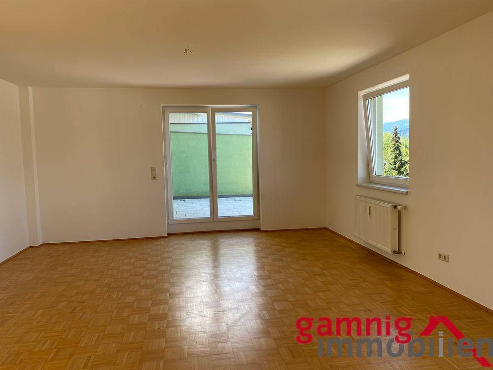 Helles Wohnzimmer mit Parkettboden und Zugang zu einem Außenbereich durch eine große Glastür.