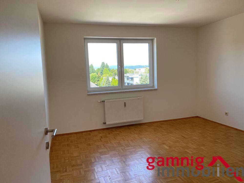 Schlafzimmer mit Parkettboden und großem Fenster, das einen weiten Blick in die Natur bietet.