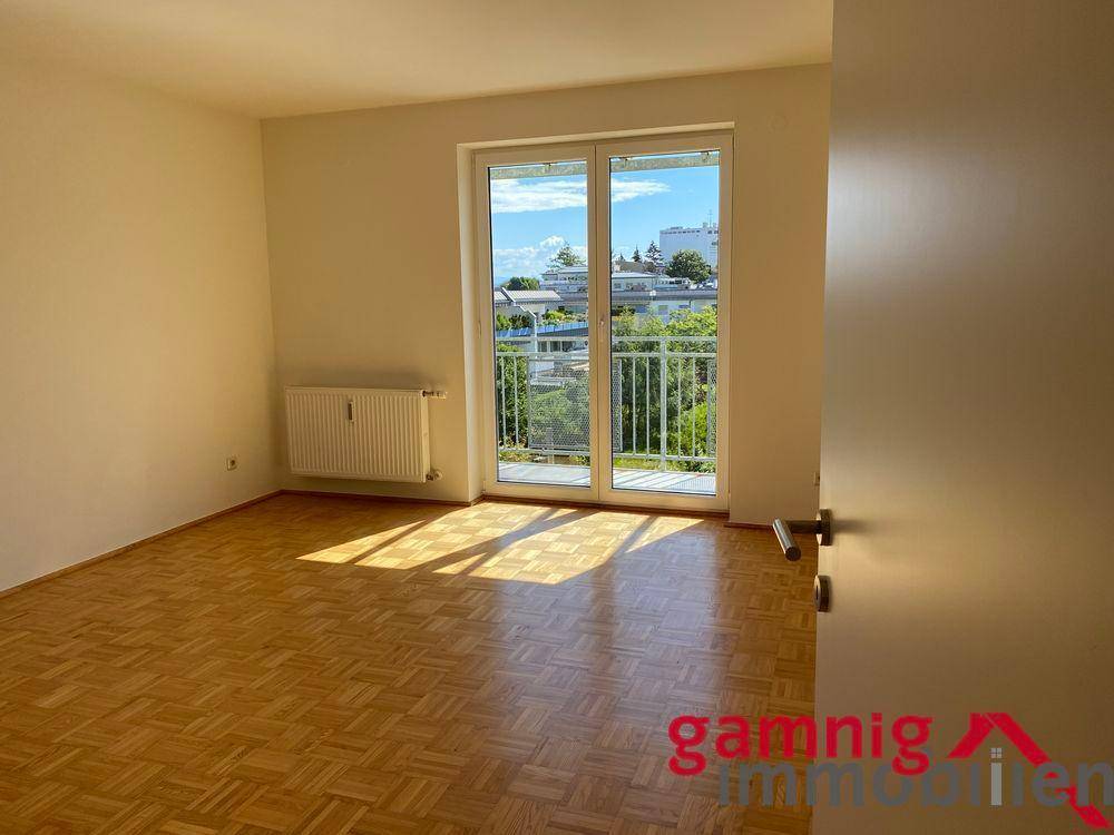 Helles Schlafzimmer mit Parkettboden und Balkonzugang, durchflutet von Sonnenlicht.