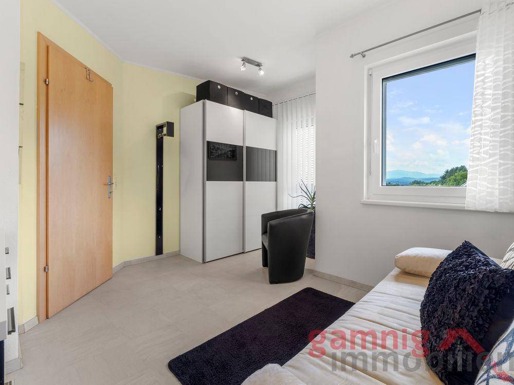 Helles Schlafzimmer mit Schrank, Sofa und Fenster mit Bergblick.