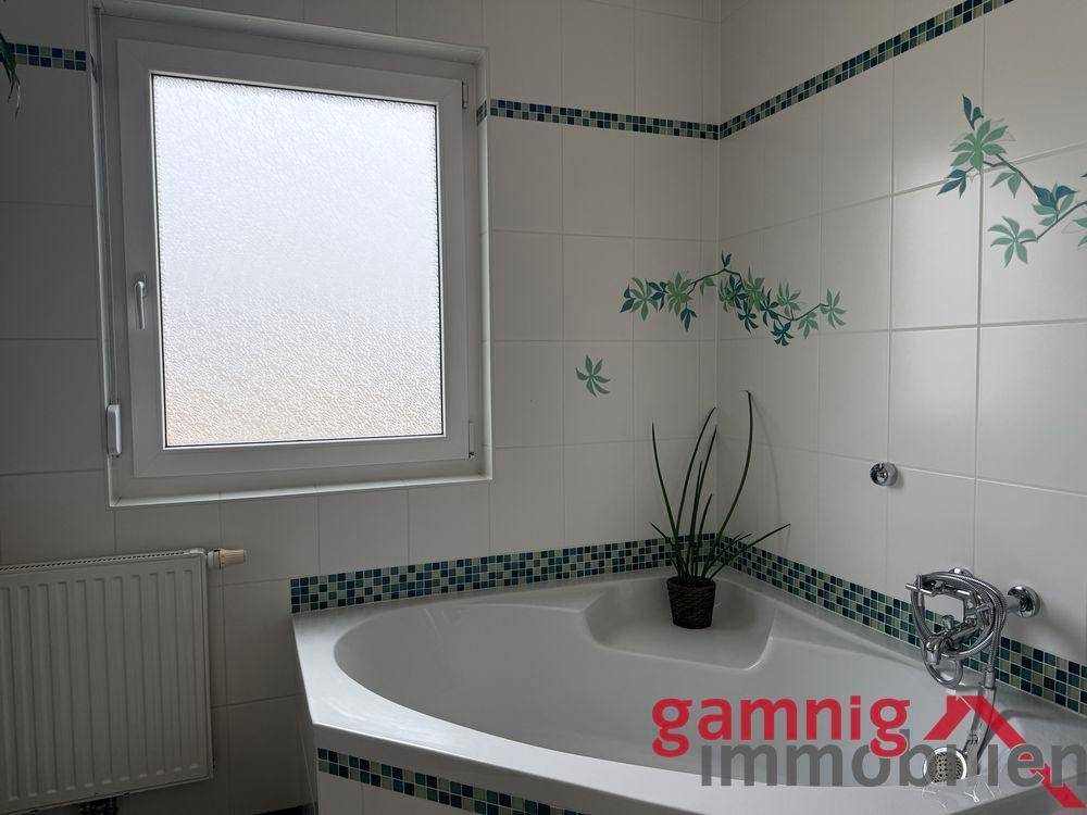 Badezimmer mit Eckbadewanne, Fenster und dekorativen grünen Fliesen.