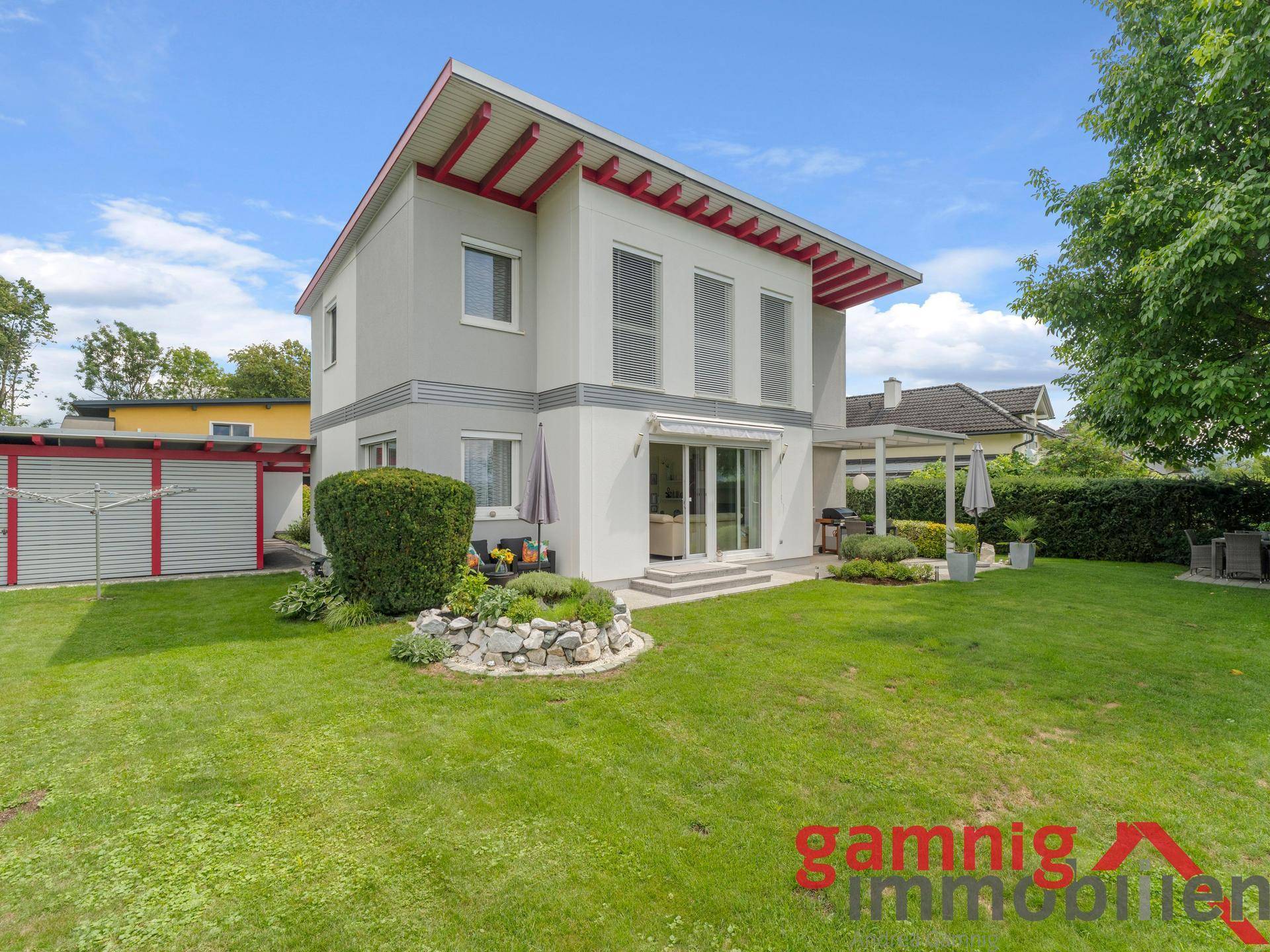 Rückansicht des modernen Hauses mit weitläufigem Rasen, Terrasse und roten Dachuntersichten.