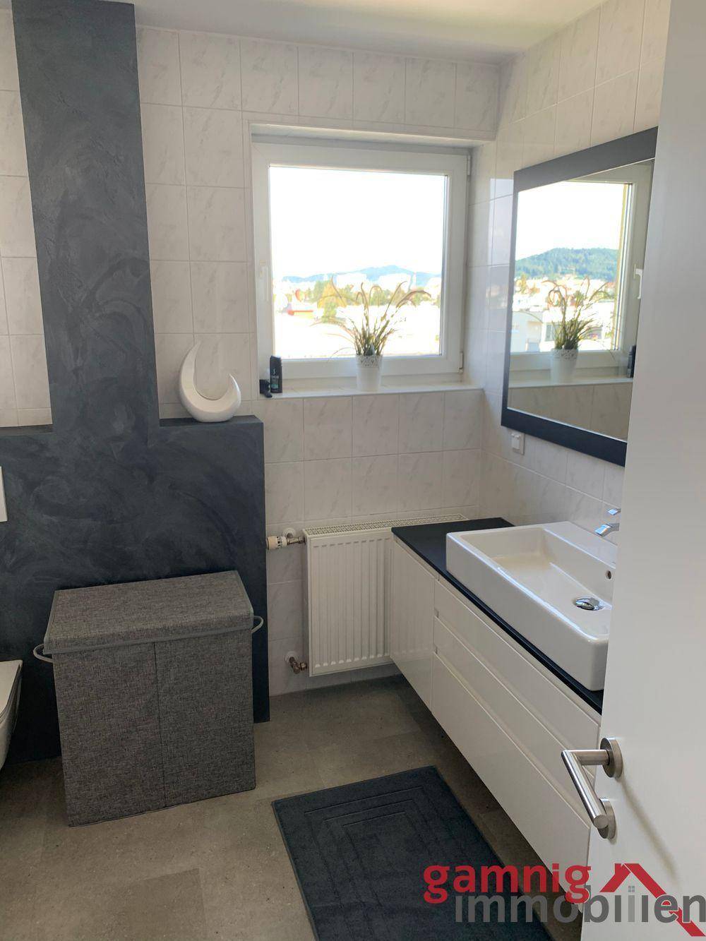 Modernes Badezimmer mit großem Fenster, Waschtisch und dunklen Akzenten an der Wand.