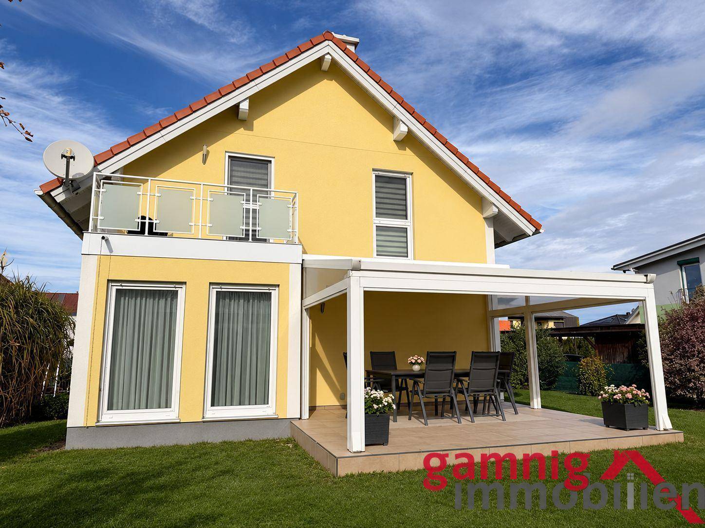 Gelbes Einfamilienhaus mit überdachter Terrasse, Balkon und gepflegtem Garten.