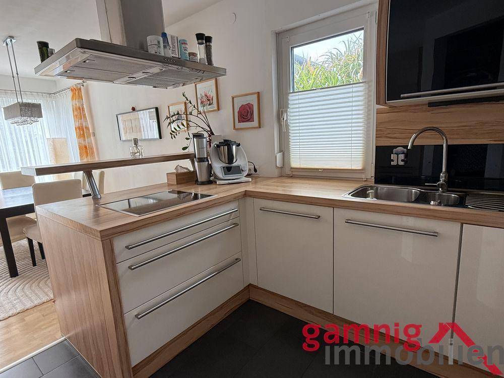 Moderne Einbauküche mit Holz-Arbeitsplatte, Induktionskochfeld und Dunstabzugshaube.