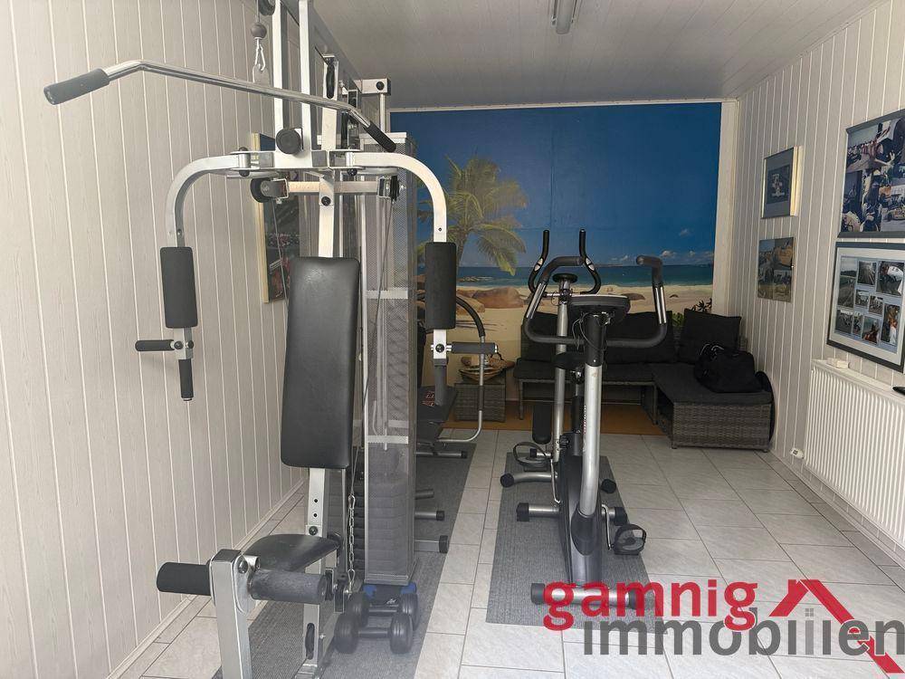 Fitnessraum mit verschiedenen Trainingsgeräten und Wandbild.