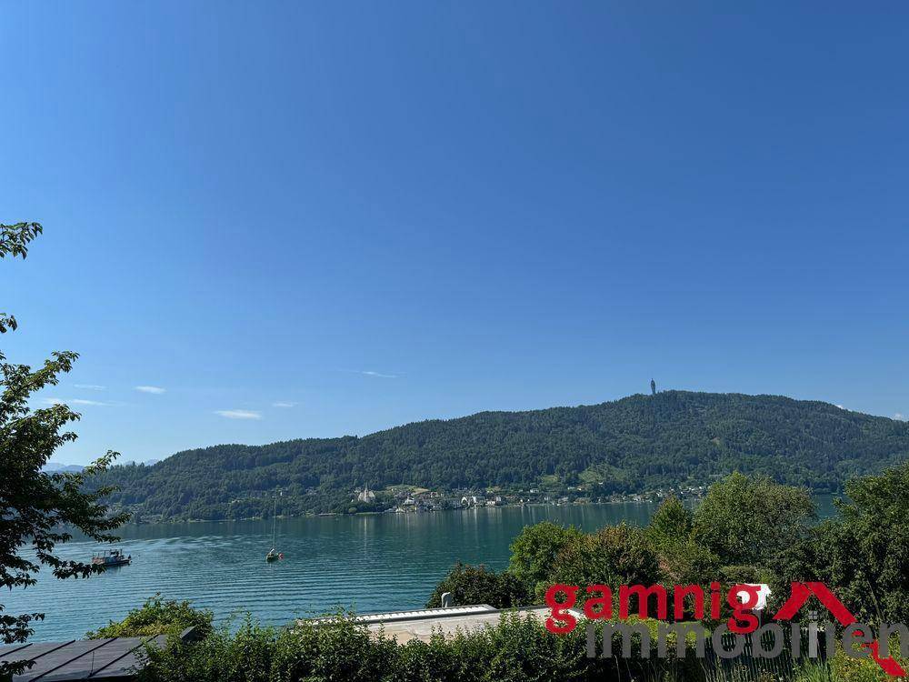 Panoramablick auf einen See mit bewaldeten Bergen unter einem klaren blauen Himmel.