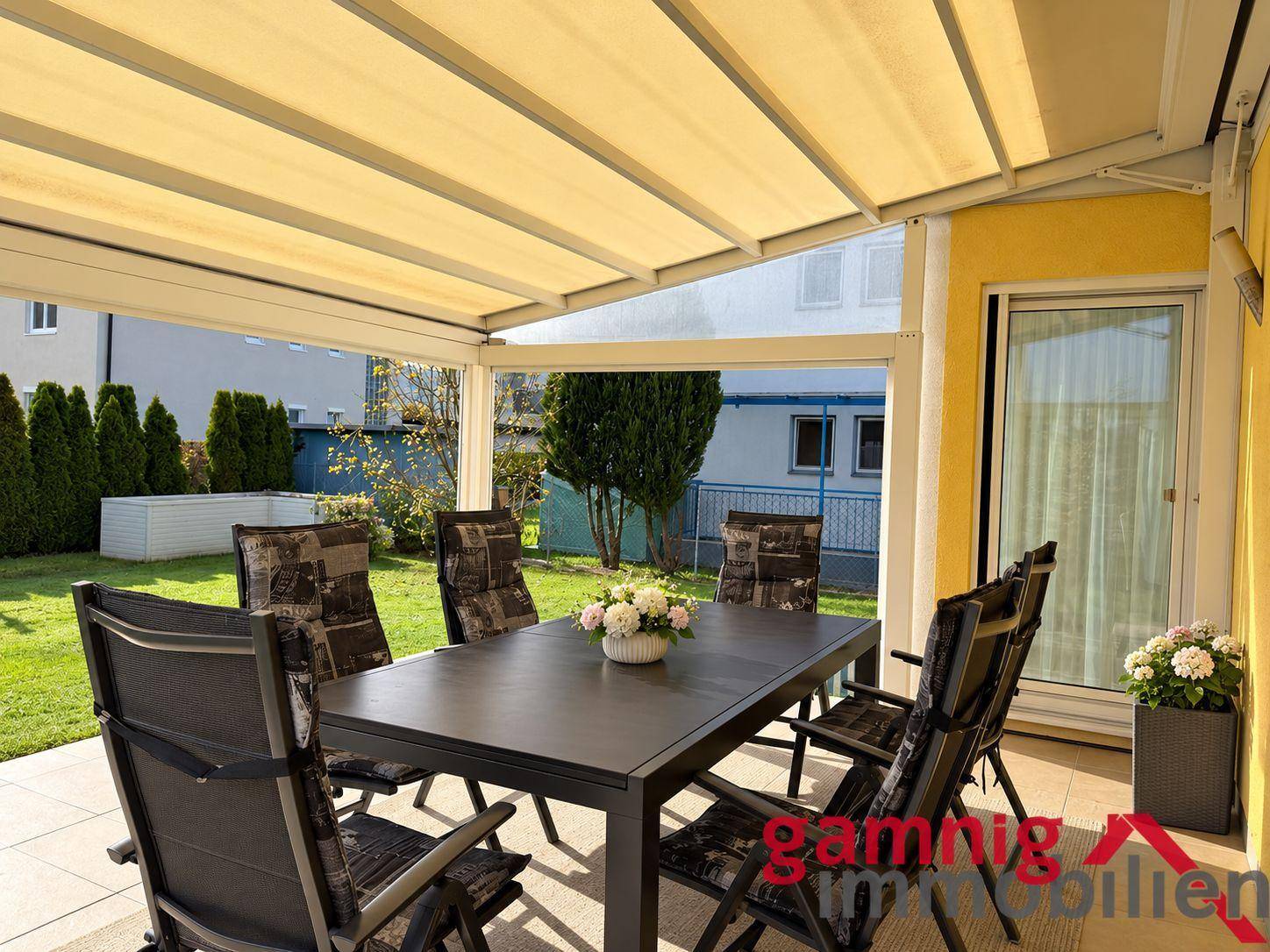 Helle, überdachte Terrasse mit Essbereich und Blick in den grünen Garten.