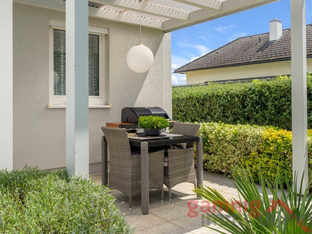 Überdachte Terrasse mit Esstisch und Grillbereich im Garten.