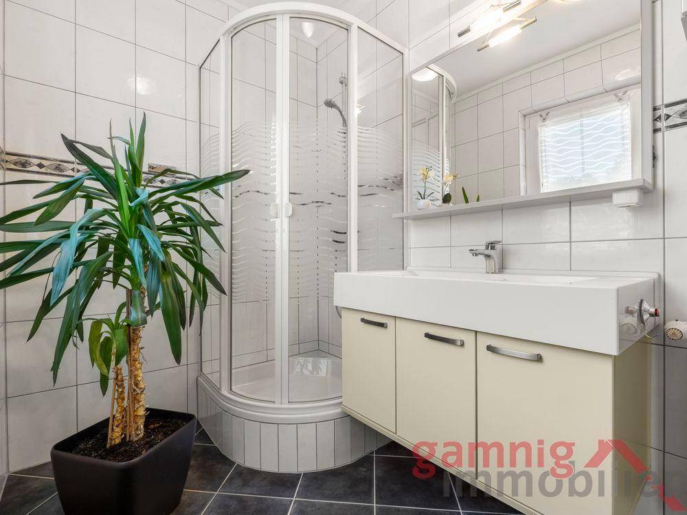Badezimmer mit Duschkabine, Waschtisch und weißen Fliesen.