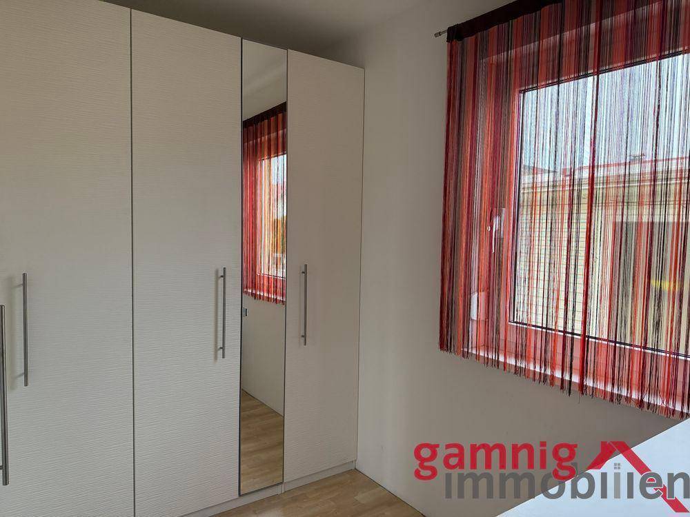 Schlafzimmer mit großem weißen Kleiderschrank und Fenster mit roten Vorhängen.