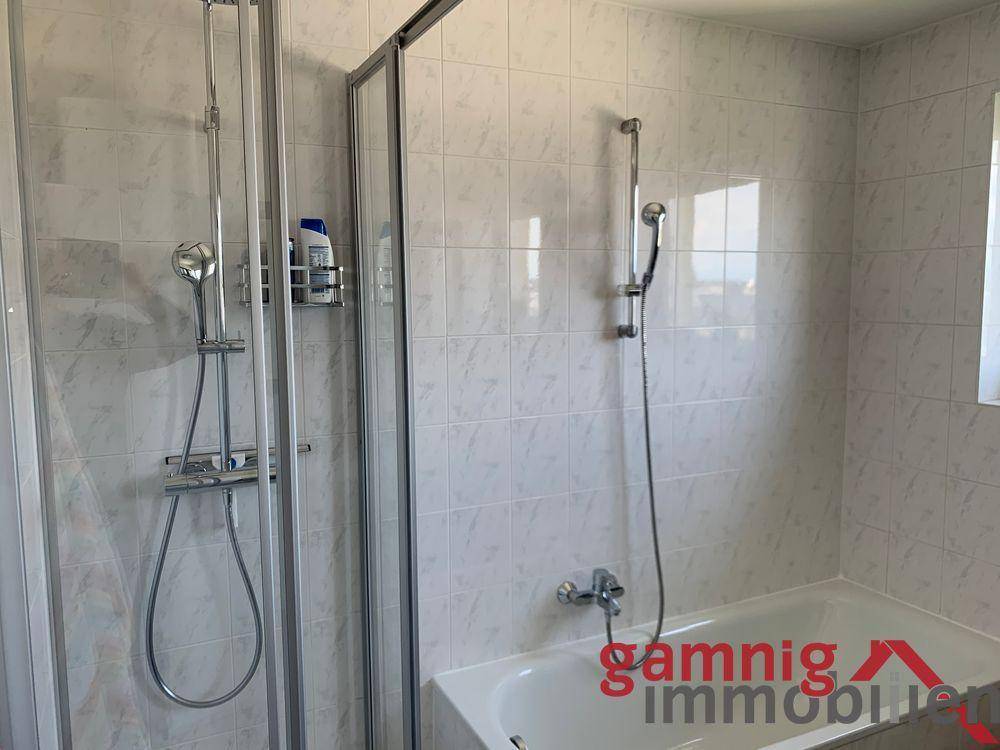 Badezimmer mit Badewanne und integrierter Dusche, komplett gefliest in hellem Design.