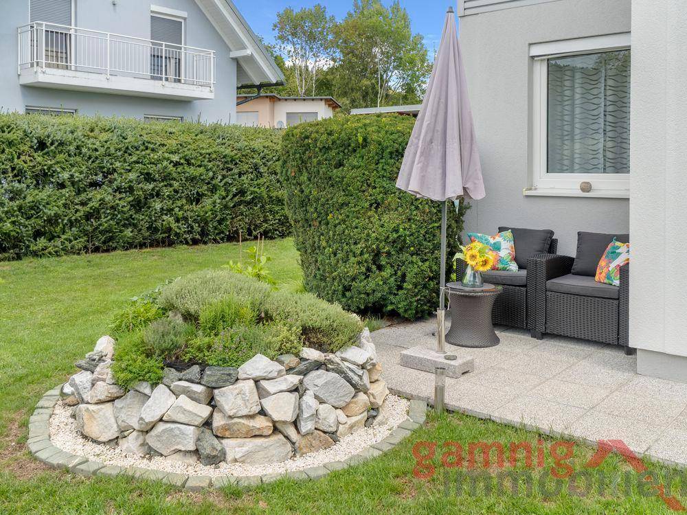 Gemütliche Sitzecke im Garten mit Sonnenschirm und dekorativem Steingarten.