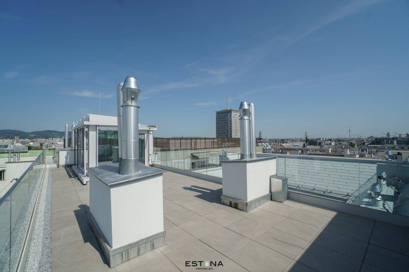 Weitläufige Dachterrasse mit Stadtblick und modernen Lüftungsschächten unter blauem Himmel.