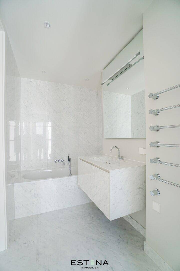 Elegantes Badezimmer mit Marmorfliesen, Badewanne und schwebendem Waschtisch mit Einzelwaschbecken.