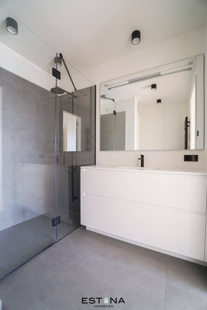 Modernes Badezimmer mit großer begehbarer Dusche, Einzelwaschbecken und grauen Fliesen.