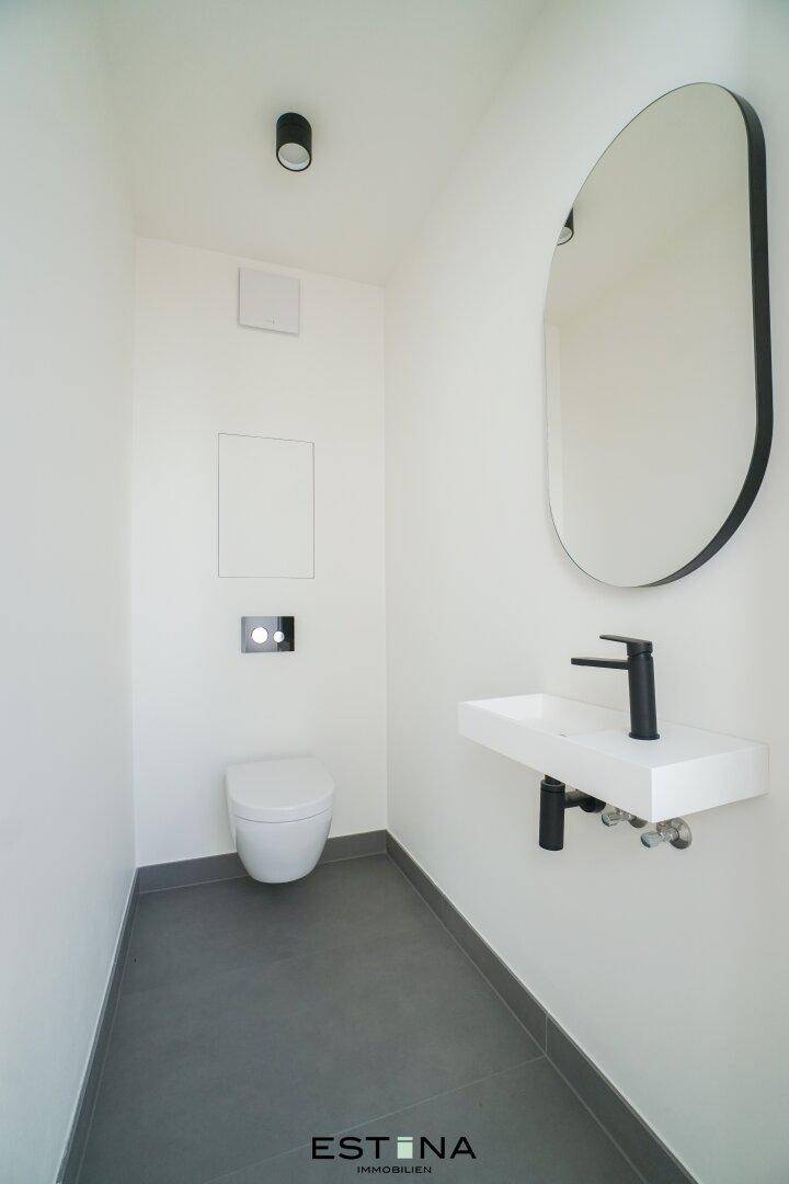 Modernes Gäste-WC mit wandhängender Toilette, kleinem Waschbecken und ovalem Spiegel.