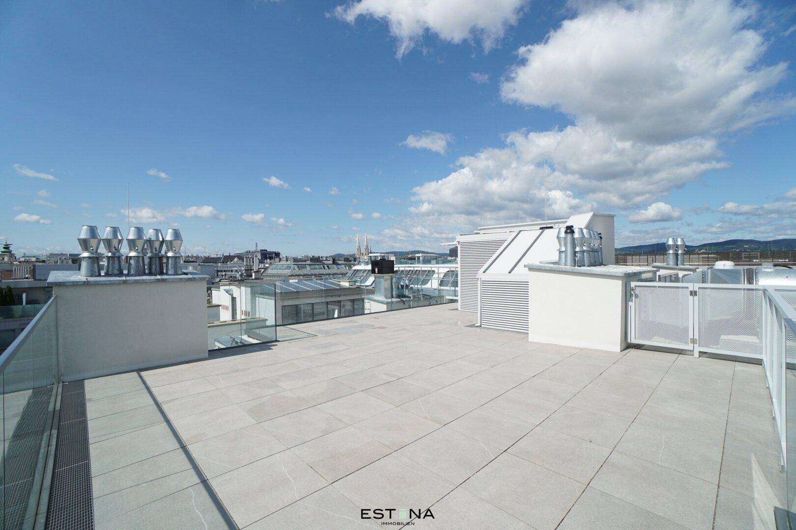 Sonnige Dachterrasse mit Fliesenboden und weitem Blick über die städtische Umgebung.