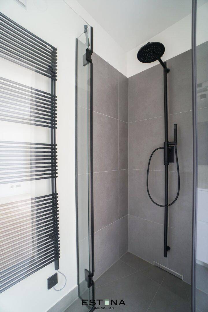 Moderne begehbare Dusche mit Regenduschkopf und dunklen Armaturen.