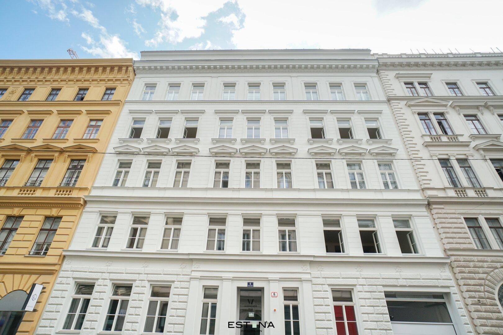 Klassische, weiß gestrichene Fassade eines Altbaus mit vielen Fenstern und dekorativen Elementen.