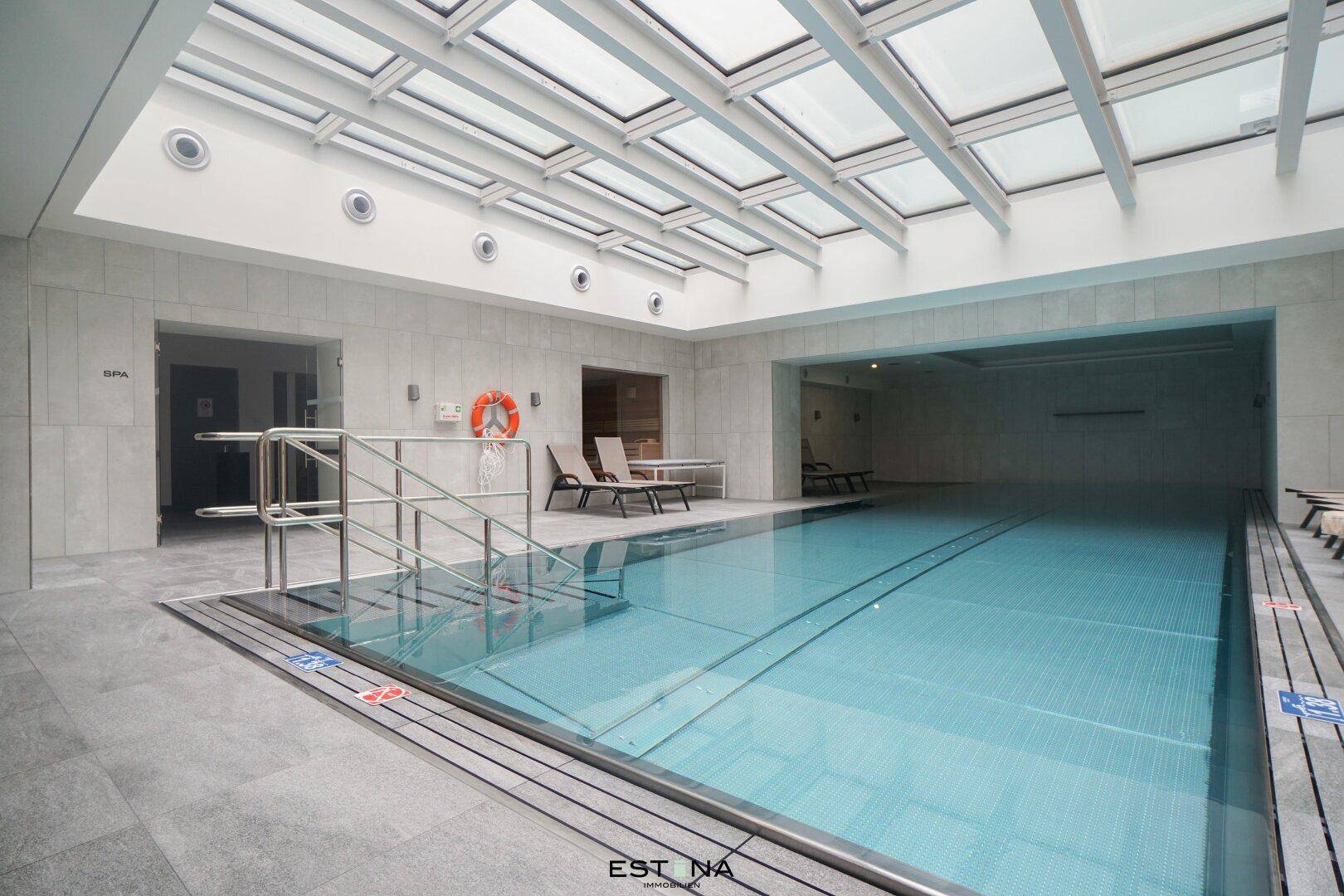 Großzügiger Innenpoolbereich mit Tageslicht durch ein Glasdach und Liegemöglichkeiten.